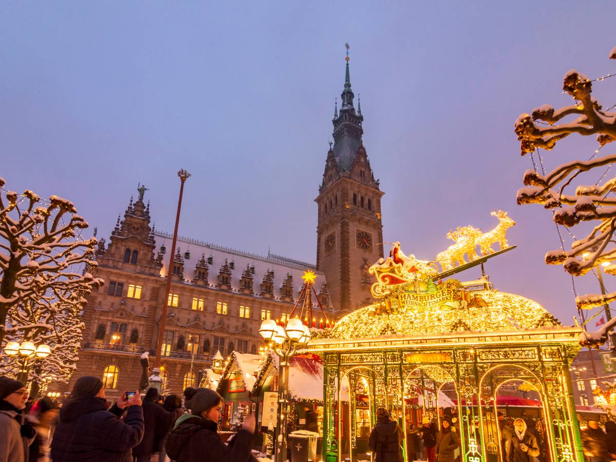 Leuchtender Weihnachtsmarkt mit Rathaus im Hintergrund.